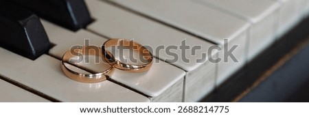 Front view of two wedding rings resting on white piano keys. The composition blends themes of love, music, and elegance. Banner with copy space.