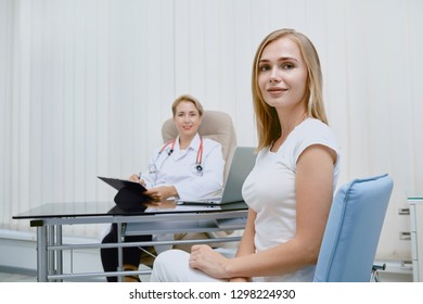 Front View Of Two Women On Medical Daily Observation In Private Clinic. Doctor Working In Hospital With Patients. Young Smiling Woman Sitting And Listening Prescription Of Doctor About Treatment.