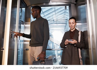 Front View Of Two Young Business People In Glass Elevator At Modern Office Building, Copy Space