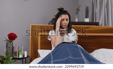 Front view of upset sick young woman which sitting in bedroom bed and drinking tea while is treated at home as cought cold with cough and headache