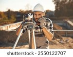 Front view, using geodetic optical level. Worker is on the construction site at daytime.