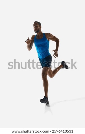 Front view vertical image of concentrated man, runner with muscular strong body in motion, running isolated on white background. Concept of sport, competition, endurance, athletics, sportive lifestyle