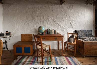 Front view of vintage room interior in traditional village country house. Old handmade furniture, school desk, wooden chairs, craft chest on stucco wall background - Powered by Shutterstock