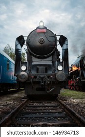 Front view of vintage steam locomotive at railway station with dramatic cloudy sky