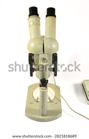 Front view of a vintage stereo microscope with binocular eyepieces isolated on a white background. Professional optical equipment for laboratory work and scientific research.