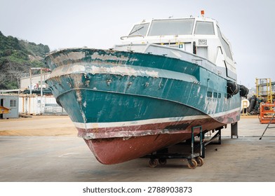 Front view of a weathered workboat positioned in a shipyard dry dock for inspection, maintenance, and hull repairs. The vessel shows signs of wear, marine growth removal, and surface preparation, illustrating maritime maintenance, ship repair operations, vessel lifecycle management, and marine engineering activities