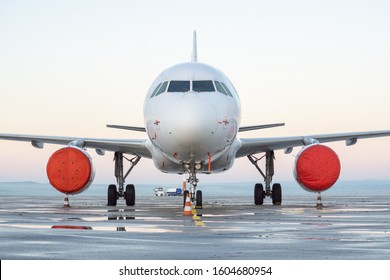 Front view of white airplane. Jet commercial aircraft on airport apron, morning daylight sky, puddles after rain. Modern technology in fast transportation, private business travel, charter flight.