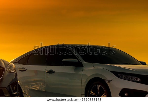 Front view of white car with luxury and modern design\
parked at parking lot with beautiful orange sunset sky. Automotive\
industry. Road trip travel. Parked car for watching sunset sky\
after work. 