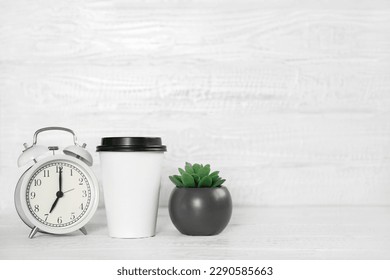 Front view white desk with alarm clock, coffee paper cup, copy space. Morning background banner with free space for text. Minimalistic concept, workspace, time to work. Blank workplace. Office mock-up