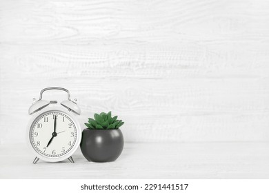Front view white desk with alarm clock, houseplant and copy space. Morning background banner with free space for text. Minimalistic concept, workspace, time to work. Blank workplace. Office mock-up.