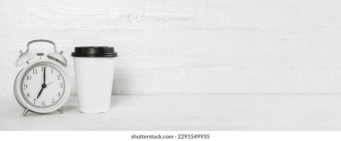 Front view white desk with alarm clock, coffee paper cup, copy space. Morning background banner with free space for text. Minimalistic concept, workspace, time to work. Blank workplace. Office mock-up