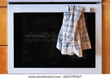 The front view of a white kitchen oven with control knobs and a plaid kitchen towel hanging from the handle.