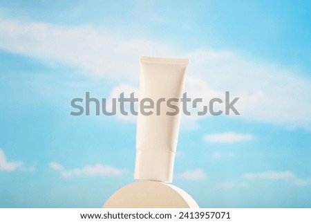 Front view of a white plastic tube displayed on a round podium on blue sky background. White cosmetic tube container for sunscreen or moisturizer, blank space for design packaging