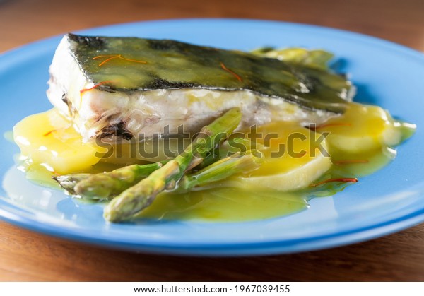 \
Front view of wild turbot steak with sliced roasted\
potatoes and green asparagus to the saffron sauce on a round blue\
dish 