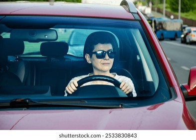 Front view of the windshield, behind which a woman is sitting behind the wheel of a car while driving with her seat belt unfastened.