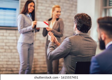 Front view of woman receiving award from businesswoman in front of business professionals applauding at business seminar in office building