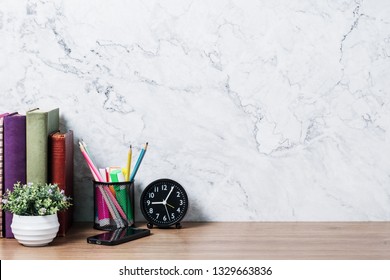 Front View Wooden Desk With Supplies, Alarm Clock, Plant And Copy Space