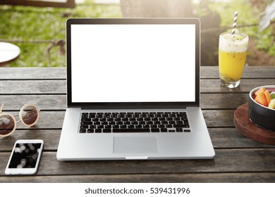 Front view of workplace of female businessman or freelancer: generic laptop computer with white copy space screen for your content on wooden table with cell phone, food and stylish sunglasses