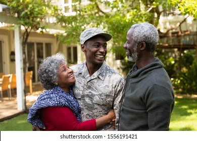 Front view of a young adult African American male soldier in the garden outside his home embracing and smiling with his parents - Powered by Shutterstock