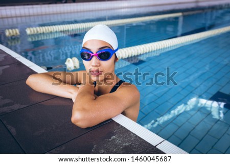 Front view of a young African-American woman wearing a swimsuit and swimming with goggles in an olympic sized pool inside a stadium