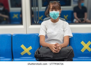 Front View Of Young Asian Backpacker Woman Wear Face Mask Sitting On The Train Seat, Look At Camera, Travel To The City By Subway Or Skytrain, COVID-19 Concept 
