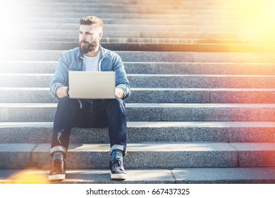 Front View. Young Bearded Businessman Sitting Outdoor On Steps And Using Laptop. Hipster Man Is Working,blogging,chatting Online,checking Email. Online Education. Social Media, Network. Lifestyle.