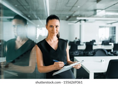 Front View Of Young Businesswoman With Clipboard In An Office, Standing.