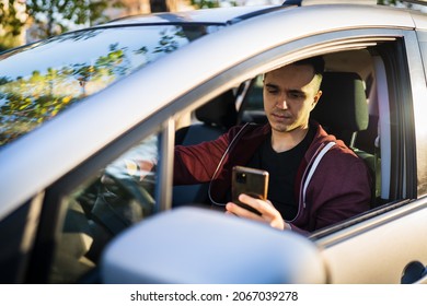 Front View Of Young Caucasian Man Checking Mobile Phone For Messages Or Navigation App For Destination While Sitting In Car Driving Or Parking Real People Travel Concept