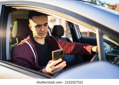 Front View Of Young Caucasian Man Checking Mobile Phone For Messages Or Navigation App For Destination While Sitting In Car Driving Or Parking Real People Travel Concept