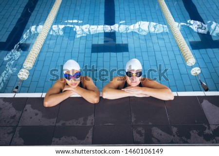 Front view of a young diverse woman and a Caucasian woman wearing a swimsuit and swimming with goggles in an olympic sized pool inside a stadium