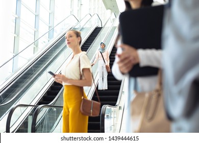 Front View Of Young Female Executive Taking Escalator While Caucasian Female Executive Look Straight Ahead  In Modern Office