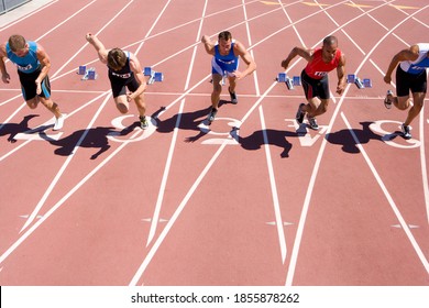 Front view of young male sprinters starting from their starting blocks at the start of a sprint race on a bright, sunny day at the track - Powered by Shutterstock