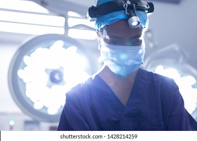 Front view of young Mixed-race female with surgical headlight performing operation in operation theater at hospital - Powered by Shutterstock