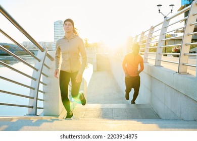 Front View Of Young Sportswoman Running Along Modern Bridge With African American Man In Activewear On Background