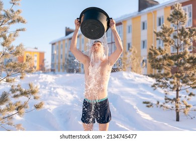 Front view of young strong-willed man tempering body, pouring water onto himself, developing resistance to cold outdoors, enjoying winter freshness outdoors in frozen sunny day.