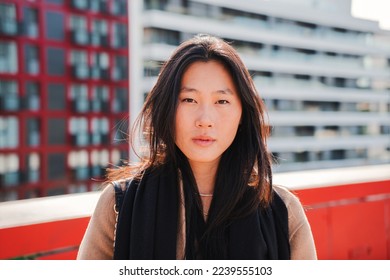 Front view of young stylish chinese woman looking serious at camera. Close up portrait of a relaxed asian lady standing outdoors at city street. High quality photo