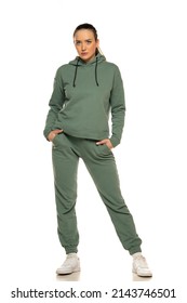 Front view of a young woman in a green tracksuit posing to a white background in the studio.