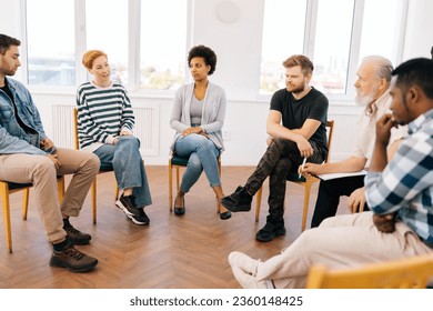 Front view of young woman telling about mental problem or addiction to other patients sitting in circle during group therapy session. Concept of mental health, psychotherapy, depression, social issues - Powered by Shutterstock