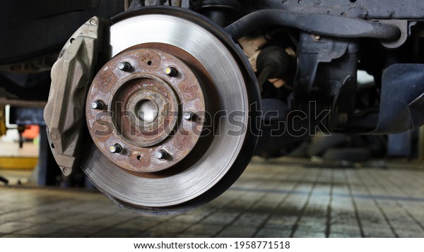 Front wheel hub\
and disc brake. Inspection of brake caliper system and suspension\
for safe driving on the background, tiled floor of the garage with\
copy space. Selective\
focus