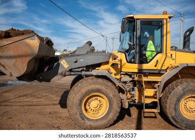 Front wheel loader operating with bucket filled with earth at urban construction site