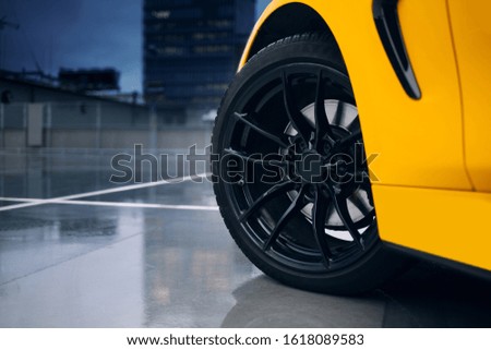 Front wheel and rims of modern sport car. Car reflection in a wet concrete floor of parking