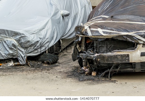 Front wheels,\
hoods and bumpers of two cars suffered during a fire. Damaged cars\
covered with a film on a city street. Accident, arson or vandalism.\
Property damaged by fire.
