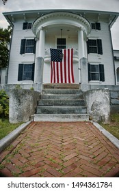 Front Of A White House With American Flag Waving. Brick Walk Up Leading Up To Front Steps.