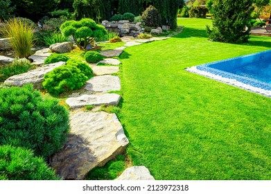 Front Yard, Landscape Design With Multicolored Shrubs Intersecting With Bright Green Lawns Behind The House Is A Modern, Garden Care Service, Green Grass With A Beautiful Yard For The Background.