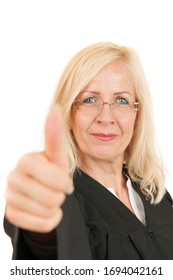 Frontal Head And Shoulder View Of A Middle-aged Blonde Woman In A Judge's Robe Showing The Thumbs Up And Smiling At The Camera Against White Background.