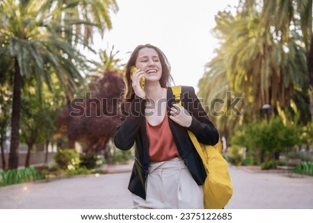 Frontal portrait of a happy woman using phone walking in a park
