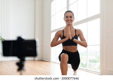 Frontal Portrait Of Positive Lady Doing Lunges Exercise In Front Of Smartphone On Tripod At Home, Free Copy Space. Beautiful Fitness Blogger Recording Video For Her Followers Having Personal Training