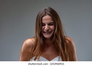 Frontal portrait of a young brown-haired girl wearing a white sheath dress laughing or smiling, unable to restrain herself from bursting into laughter - Shutterstock ID 2253960921