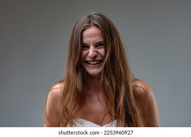 Frontal portrait of a young brown-haired girl wearing a white sheath dress laughing or smiling, unable to restrain herself from bursting into laughter - Shutterstock ID 2253960927