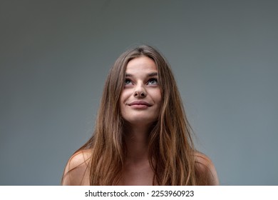 Frontal portrait of a young brown-haired young woman wearing a white sheath dress looking up because she sees something or because of her inventive - Shutterstock ID 2253960923